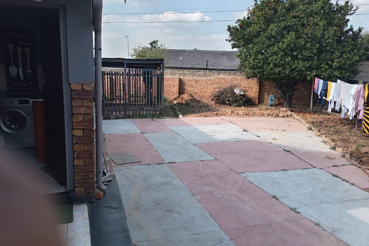 Rear exterior area featuring a paved patio, brick boundary wall, and metal security gate, offering potential for landscaping and outdoor improvement.