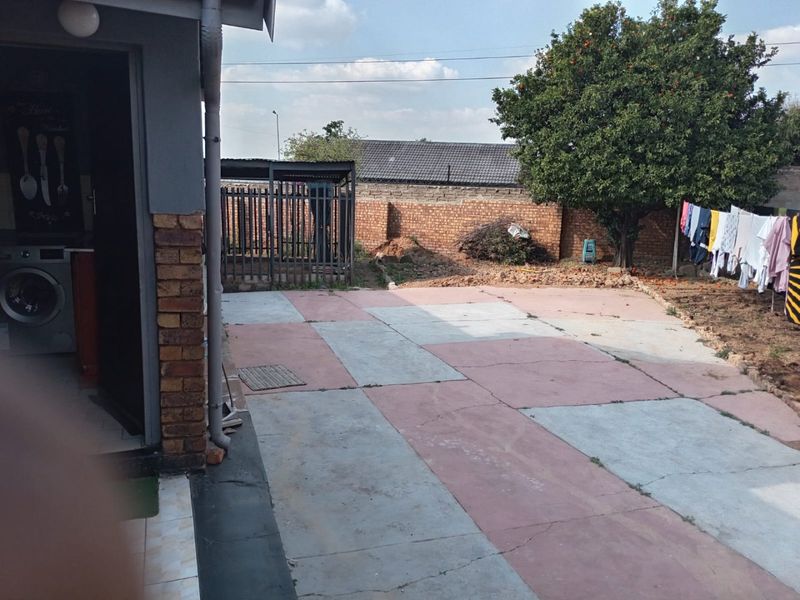 Rear exterior area featuring a paved patio, brick boundary wall, and metal security gate, offering potential for landscaping and outdoor improvement.