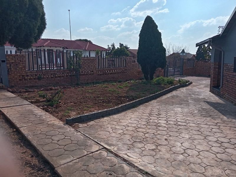 Front exterior view featuring a paved driveway, brick boundary wall with metal fencing, and a garden area.