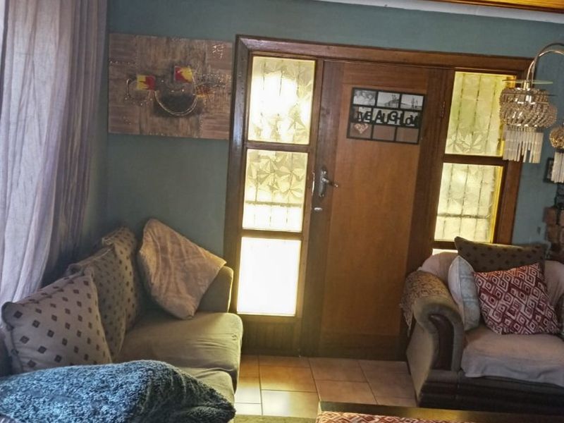 A living room featuring a warm timber tongue and groove ceiling, tiled flooring, and a classic timber-framed glass entrance door.