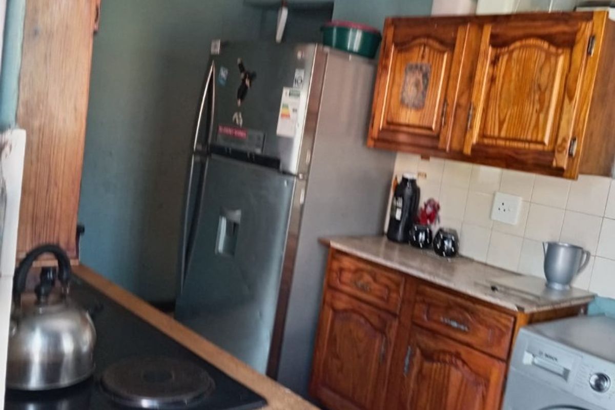 A functional kitchen featuring wooden cabinetry, tiled backsplash, and a built-in hob, offering potential for modernization and aesthetic updates.