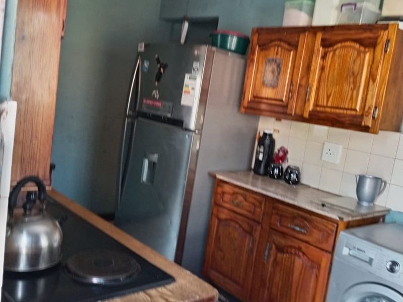 A functional kitchen featuring wooden cabinetry, tiled backsplash, and a built-in hob, offering potential for modernization and aesthetic updates.