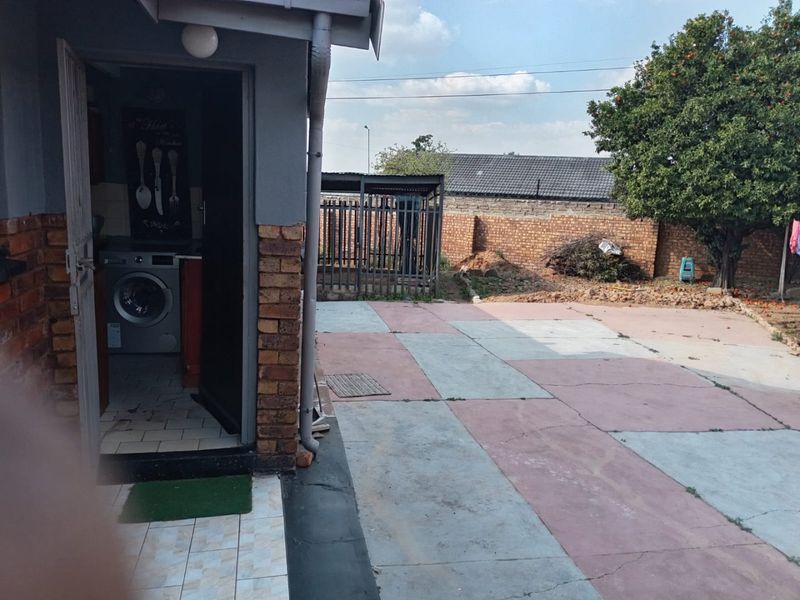 A rear exterior view showing a paved patio area, brick boundary wall, and access to a utility space.
