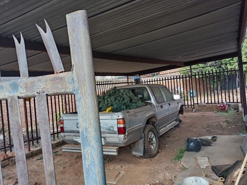 A covered outdoor parking area or carport featuring a corrugated metal roof, steel support structure, and perimeter security fencing.