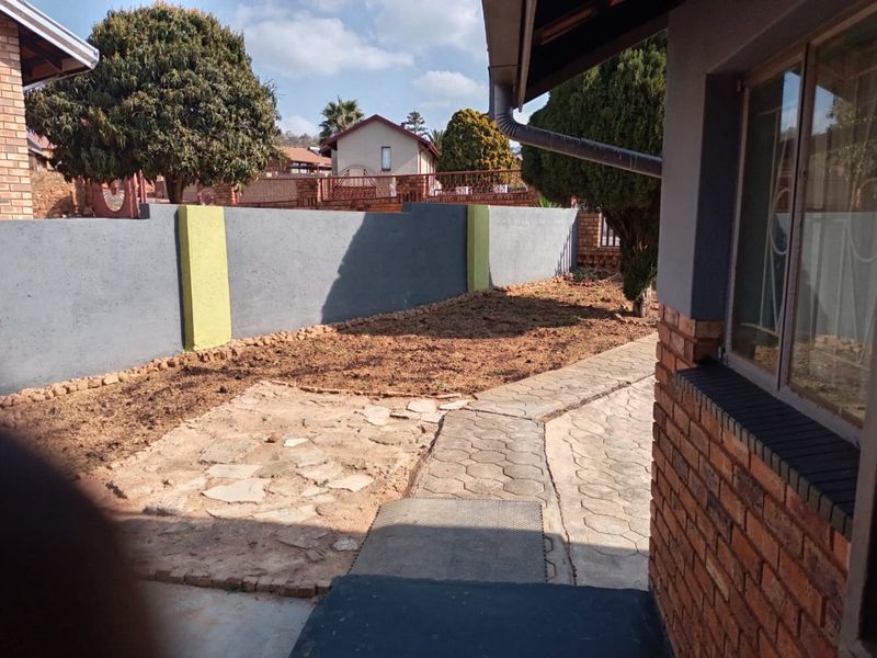 A rear garden area featuring a perimeter wall, paved walkway, and stone patio, offering potential for landscaping and outdoor improvement.