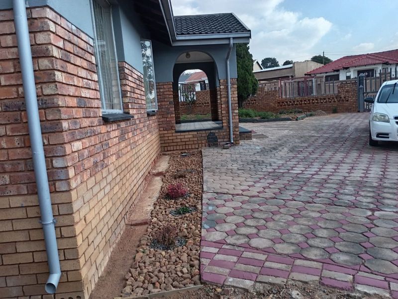 Front exterior view of a face brick house featuring a paved driveway, covered entrance porch, and perimeter boundary wall.