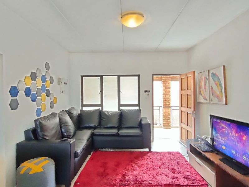 A living room area featuring tiled flooring, a ceiling light fixture, and access to an outdoor space through a doorway.