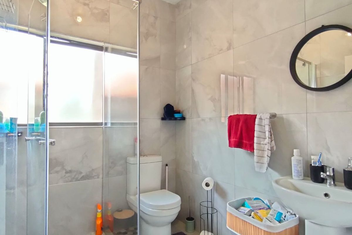 A modern bathroom featuring a glass-enclosed shower, pedestal basin, and neutral wall tiling, providing a clean and functional space.