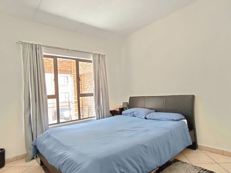 A bedroom featuring tiled flooring, neutral walls, and an aluminium-framed window providing natural light.
