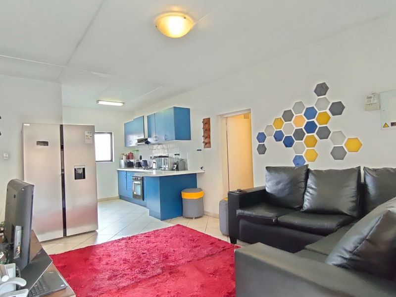 Open-plan living area featuring a functional kitchen with blue cabinetry, integrated oven and hob, and tiled flooring throughout the combined space.
