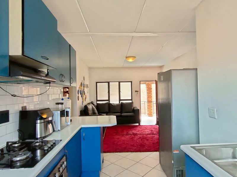 Open-plan kitchen and living area featuring blue cabinetry, gas hob, and tiled flooring, leading to an outdoor balcony space.