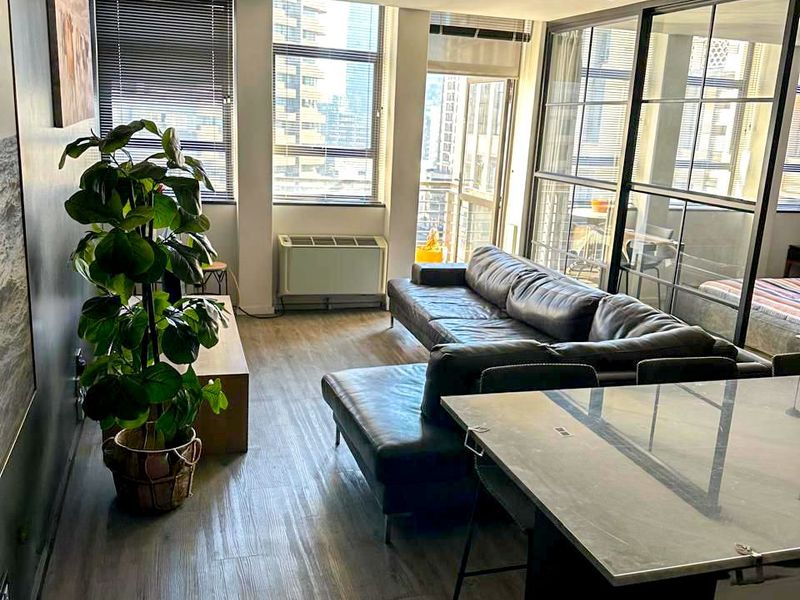 Modern open-plan living area featuring wood-look laminate flooring, a sleek black metal-framed glass partition, and large windows providing ample natural light.