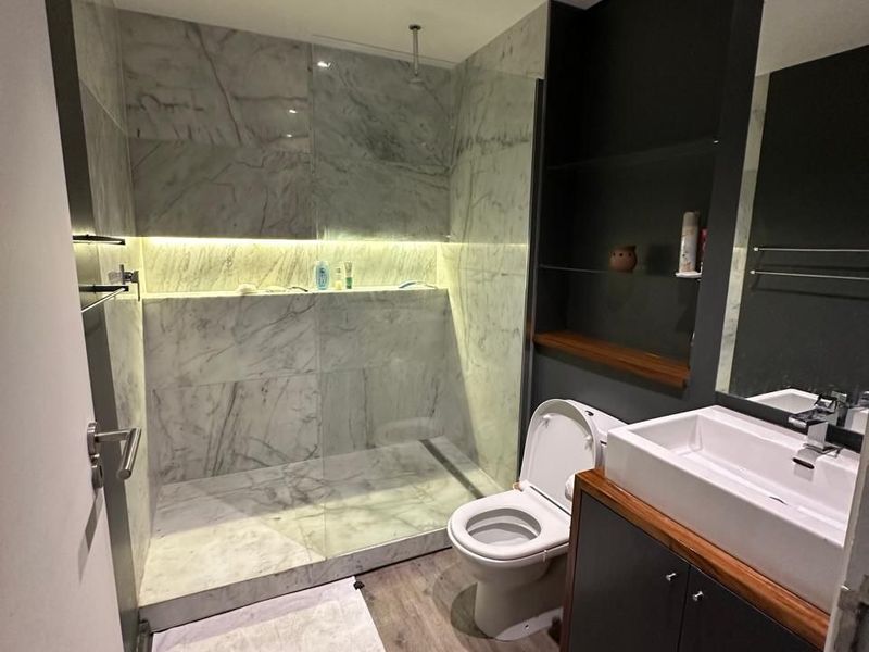 Modern bathroom featuring a spacious walk-in shower with marble-look tiling, integrated LED lighting, a sleek vanity unit, and contemporary fixtures.