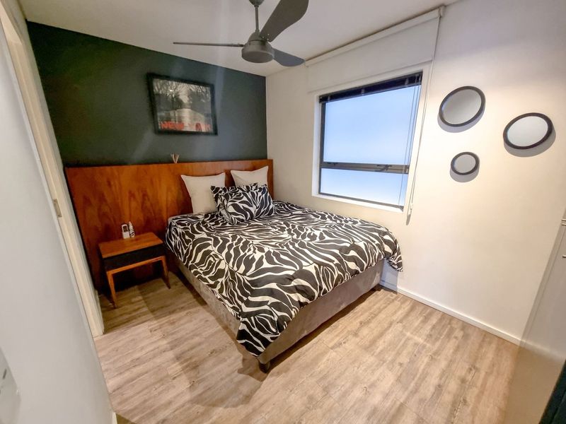 A well-maintained bedroom featuring laminate flooring, a ceiling fan, and a decorative timber headboard panel against a dark accent wall.