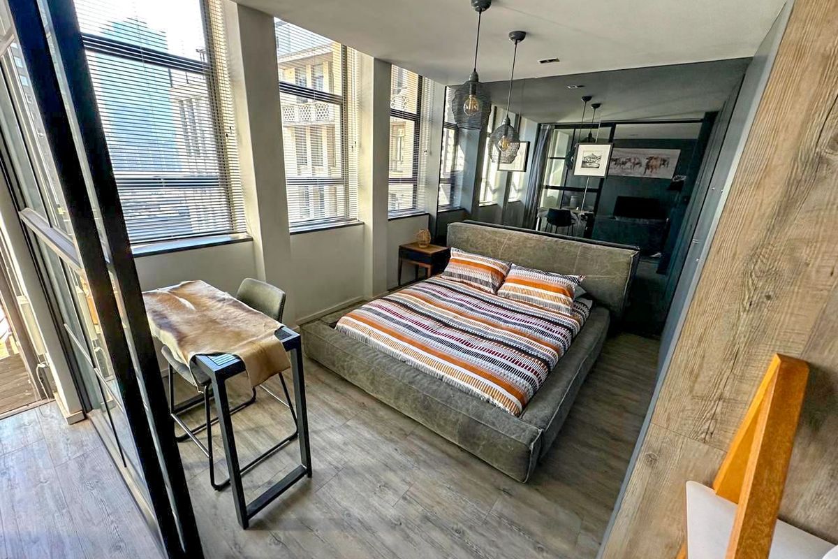 Modern bedroom featuring laminate flooring, large windows with venetian blinds, and a feature mirrored wall, creating a bright and contemporary living space.