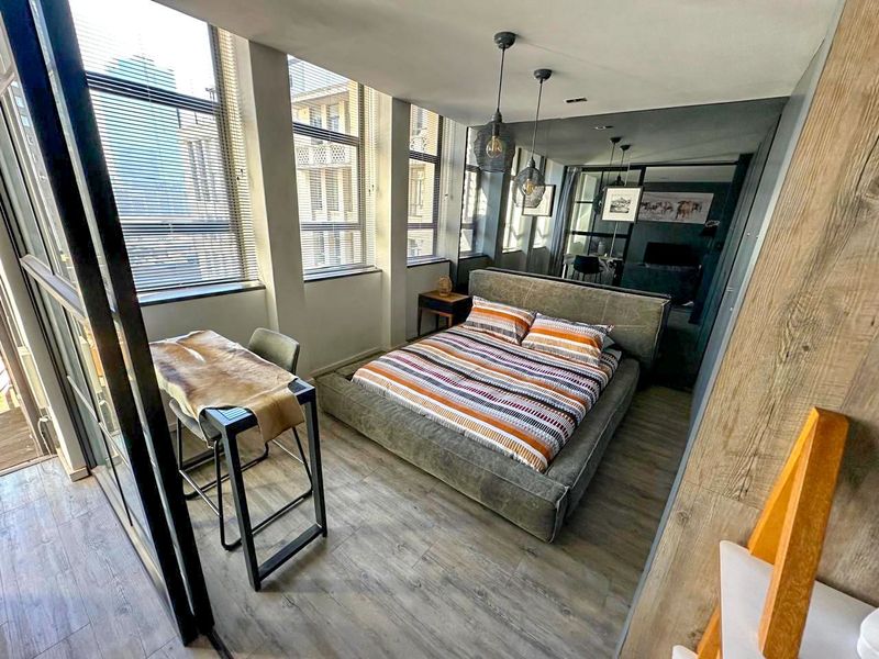 Modern bedroom featuring laminate flooring, large windows with venetian blinds, and a feature mirrored wall, creating a bright and contemporary living space.