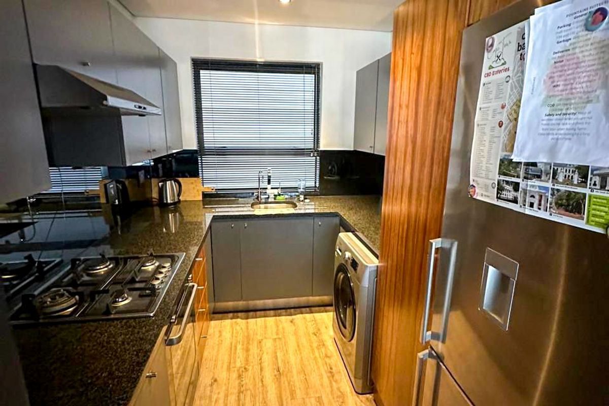 A compact, modern kitchen featuring granite countertops, gas hob, extractor fan, and integrated cabinetry with wood-look tile flooring.
