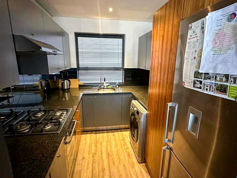 A compact, modern kitchen featuring granite countertops, gas hob, extractor fan, and integrated cabinetry with wood-look tile flooring.
