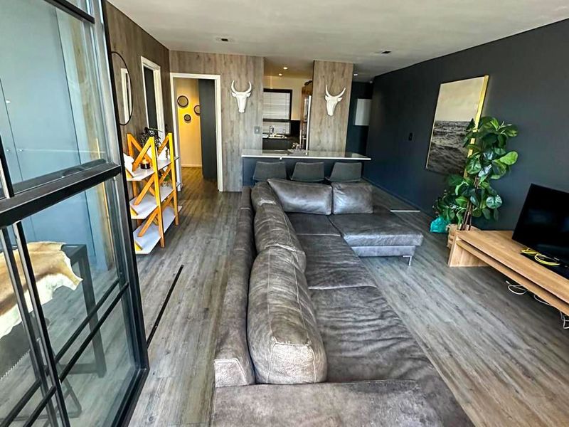 Modern open-plan living area featuring wood-look flooring, a stylish black metal glass partition, and a seamless transition to the kitchen breakfast bar.