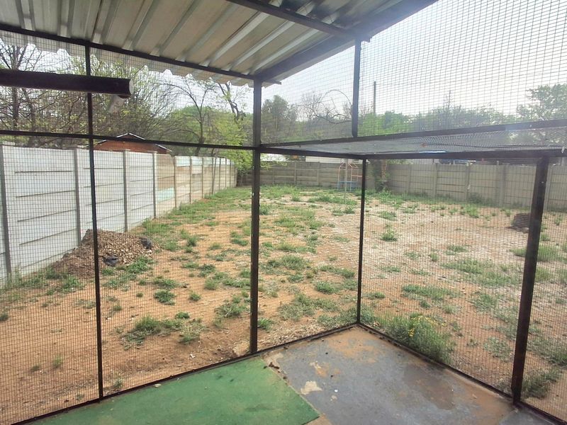 A covered outdoor patio area enclosed with metal mesh, overlooking a large, undeveloped backyard with precast concrete perimeter fencing.