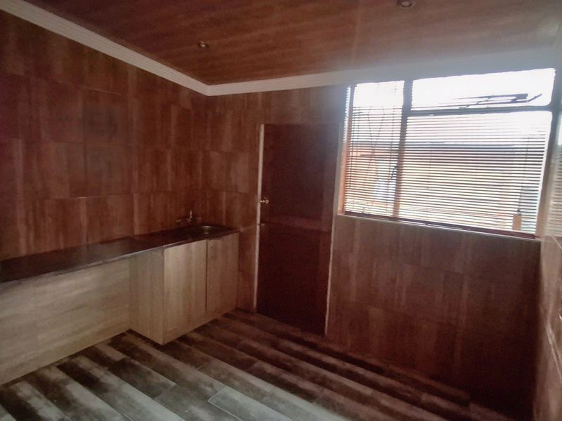 A functional scullery or utility area featuring built-in cabinetry, a sink, tiled wall finishes, and wood-look flooring.