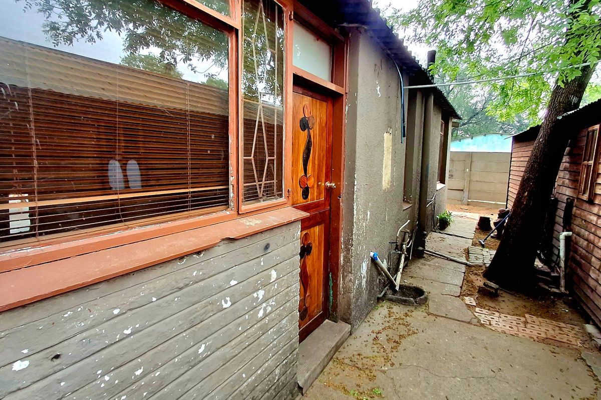Rear exterior view of the property showing a timber door, window frames, and concrete pathway alongside a wooden shed structure.
