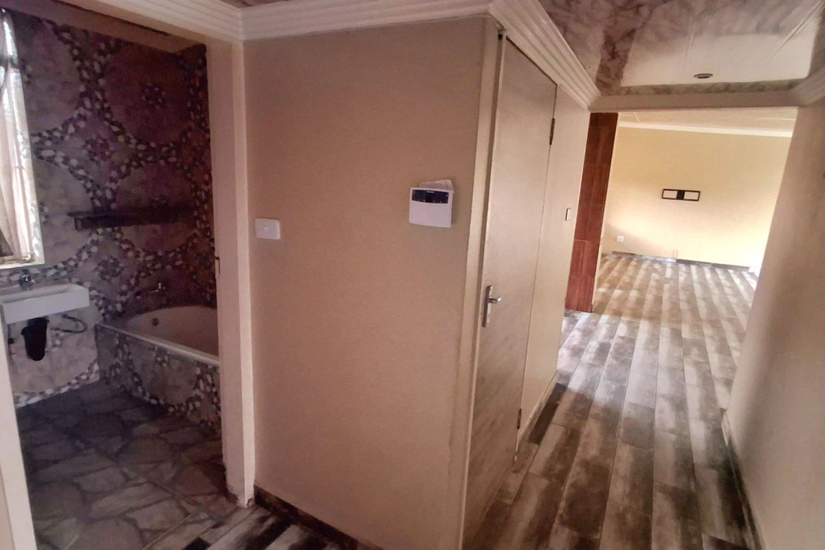 A bathroom featuring a built-in bathtub and wall-mounted basin, connected to a hallway with wood-look tiled flooring and a security alarm system.