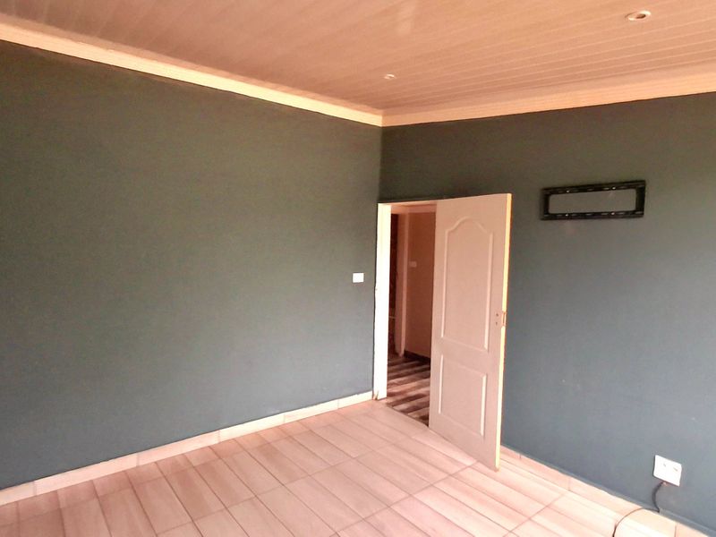 A clean, empty bedroom featuring tiled flooring, a panelled ceiling with recessed lighting, and dark-toned walls.