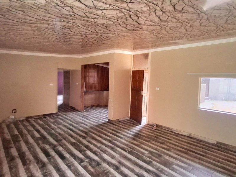 Spacious open-plan living area featuring distinctive decorative ceiling finishes and modern laminate flooring, offering a versatile layout for various living arrangements.