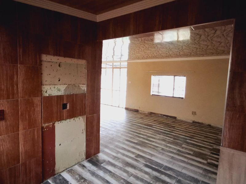 An open-plan living area featuring wood-look tiled flooring and partial wall tiling, currently requiring finishing and repairs to the wall surfaces.