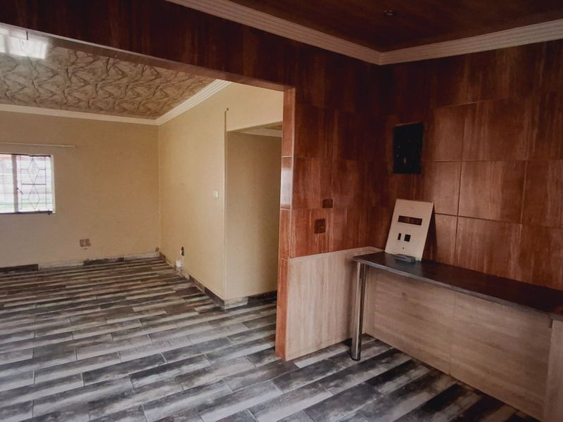 An empty open-plan living area featuring wood-look tile flooring, tiled wall accents, and a built-in counter, requiring minor electrical finishing.