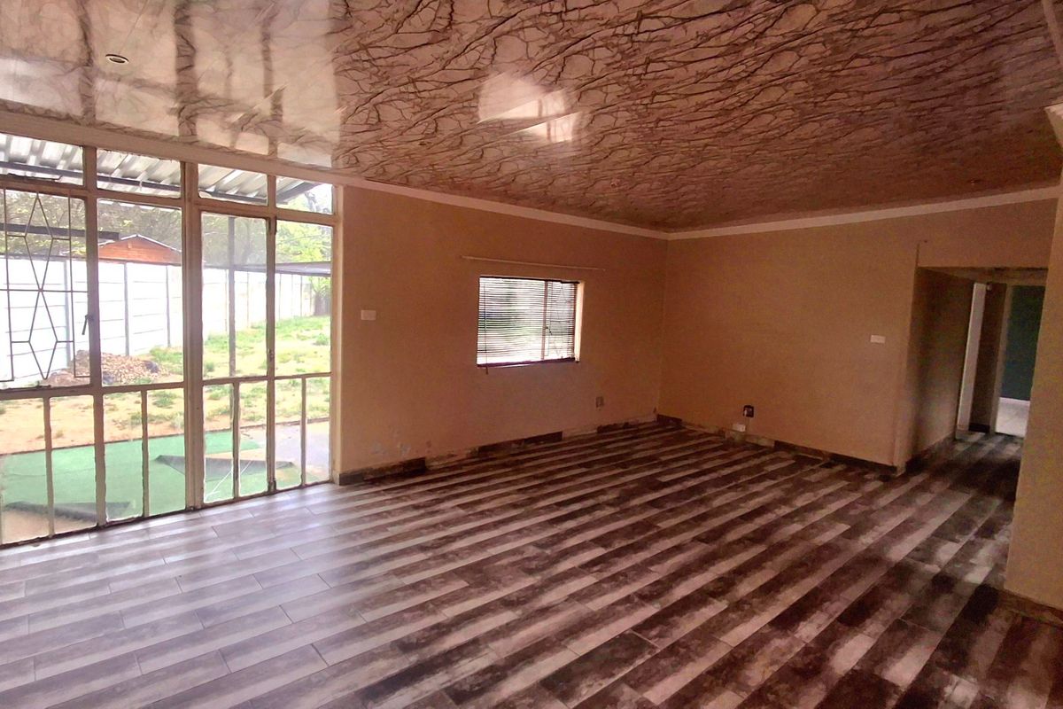 An empty living room featuring laminate flooring, decorative ceiling panels, and large glass sliding doors providing access to the outdoor area.
