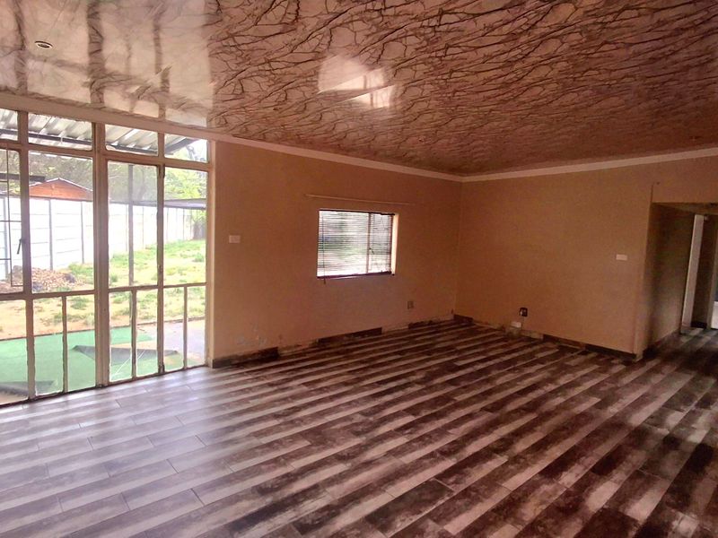 An empty living room featuring laminate flooring, decorative ceiling panels, and large glass sliding doors providing access to the outdoor area.