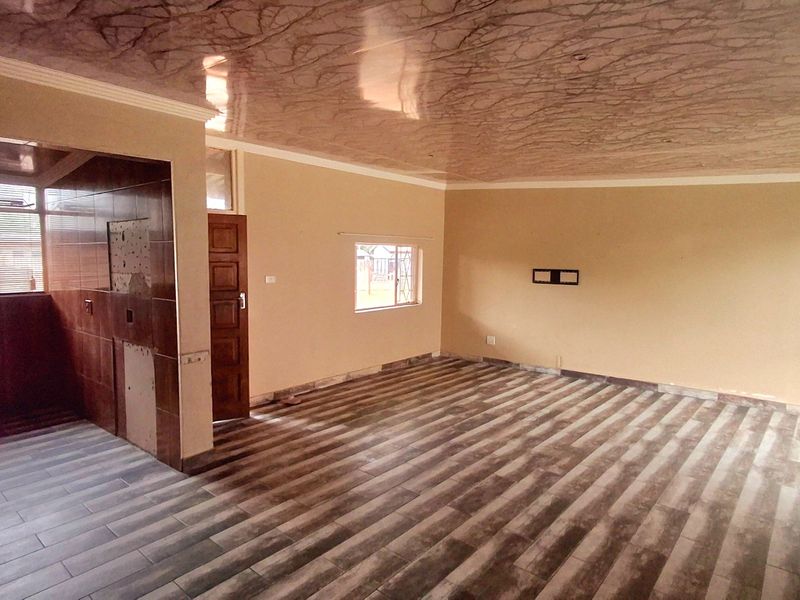 An empty open-plan living area featuring wood-look laminate flooring, a unique patterned ceiling, and a tiled partition wall with security bars on the windows.