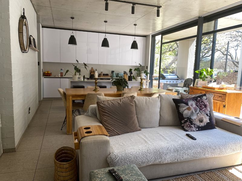 Modern open-plan living and kitchen area featuring an exposed concrete ceiling, sleek white cabinetry, and large sliding glass doors leading to an outdoor space.