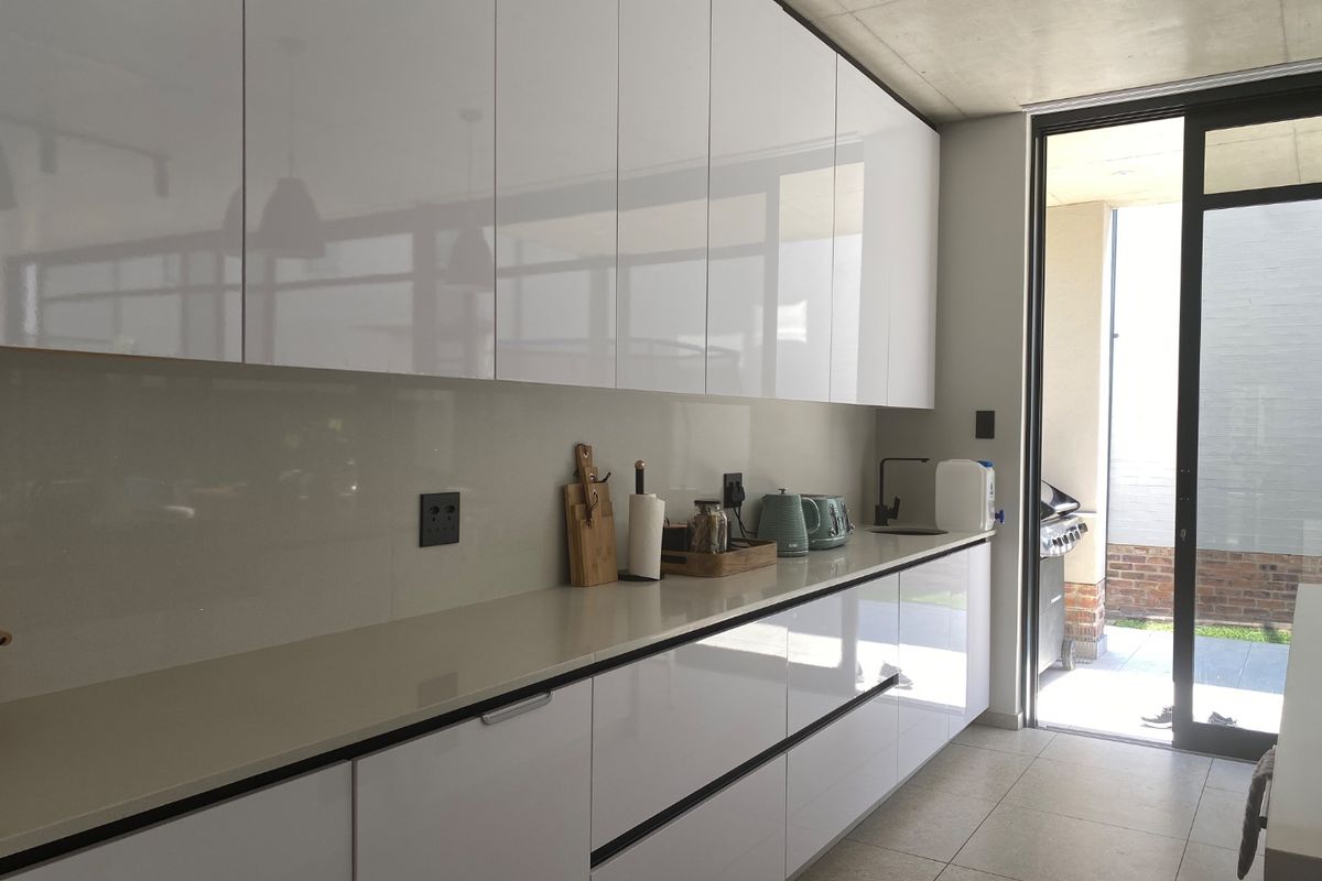Modern kitchen featuring sleek white cabinetry, stone countertops, glass splashback, and direct access to an outdoor patio area.
