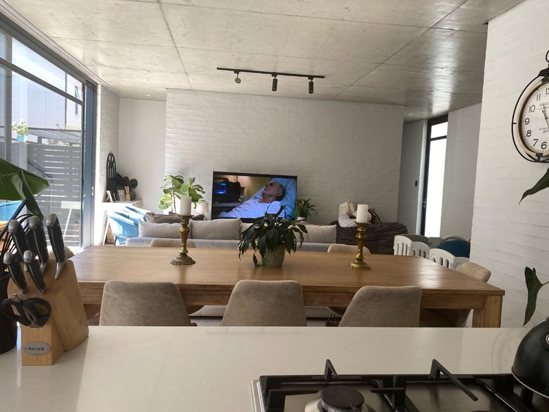 An open-plan living and dining area featuring an exposed concrete ceiling, painted brick feature wall, and a modern kitchen with a gas hob.