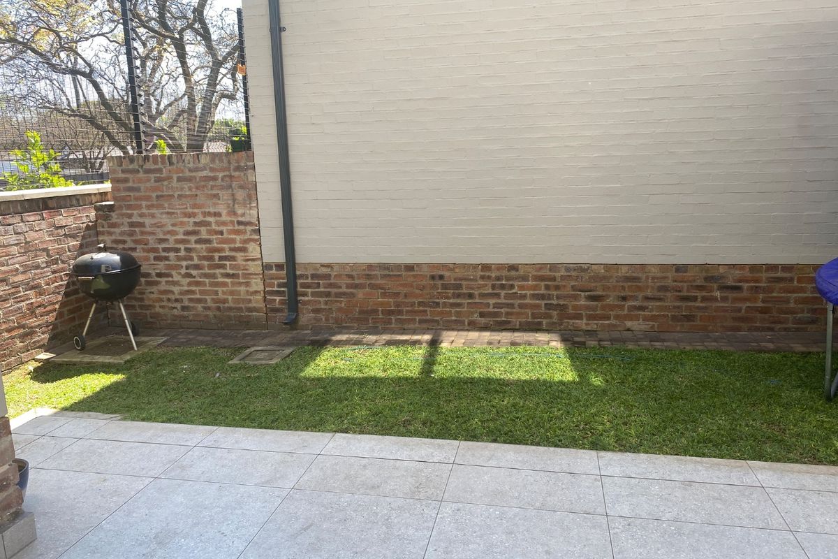 A private rear courtyard featuring a paved patio area, a small lawn, and a combination of painted brick and exposed brick boundary walls.
