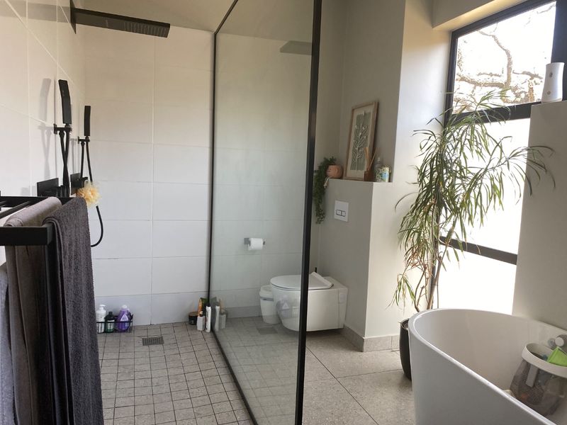 Modern bathroom featuring a spacious walk-in shower with black fixtures, a wall-mounted toilet, and a sleek freestanding bathtub with large window views.