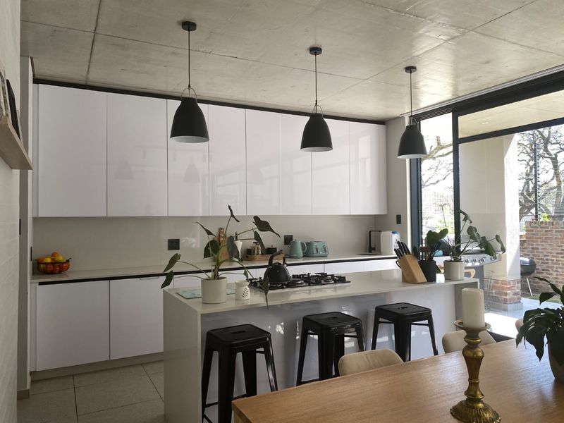 Modern kitchen featuring white gloss cabinetry, a central island with a gas hob, exposed concrete ceilings, and seamless access to an outdoor patio area.