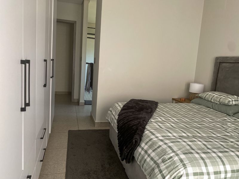 A well-maintained bedroom featuring neutral walls, tiled flooring, and ample built-in cupboard storage, with a view leading into an adjacent hallway.