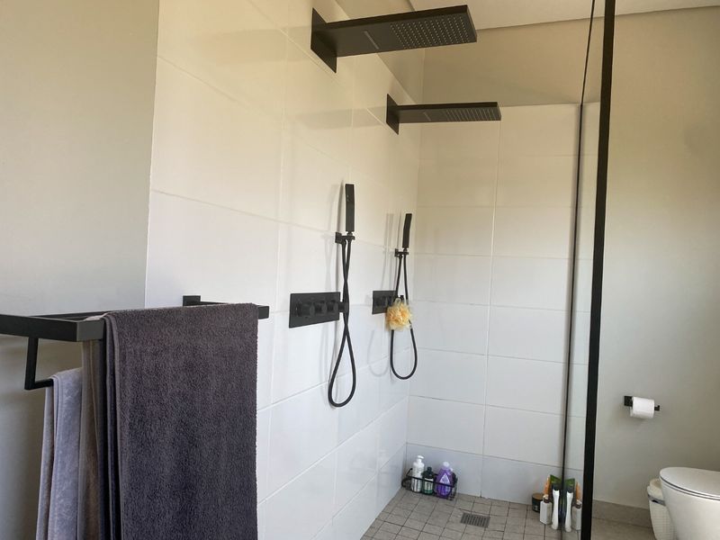Modern bathroom featuring a spacious walk-in shower with dual rainfall and handheld shower heads, sleek black fixtures, and contemporary wall tiling.