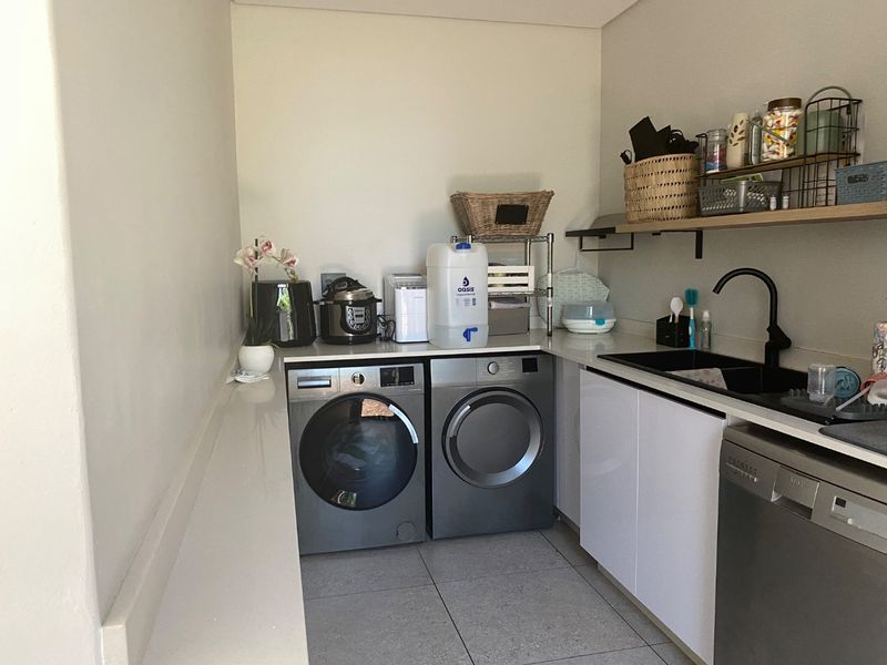 A modern, functional laundry room featuring sleek white cabinetry, stone countertops, a black sink with matching tap, and space for laundry appliances.