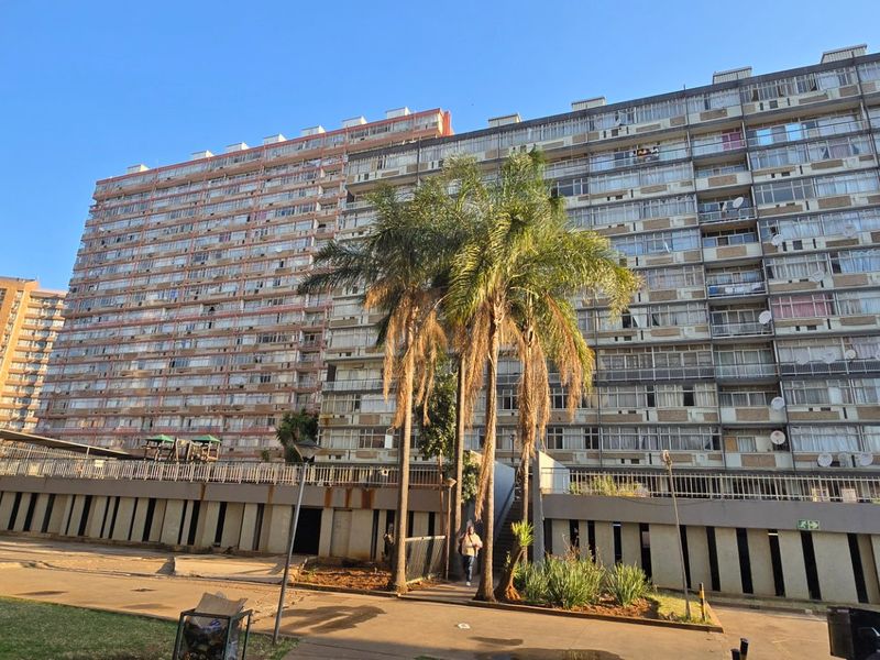 Exterior view of a large multi-story apartment complex featuring a paved driveway and concrete retaining wall structure.