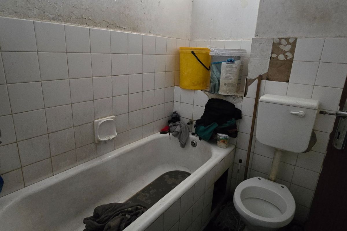 A dated bathroom featuring a bathtub and toilet, requiring significant renovation and repair to the wall finishes and tiling.