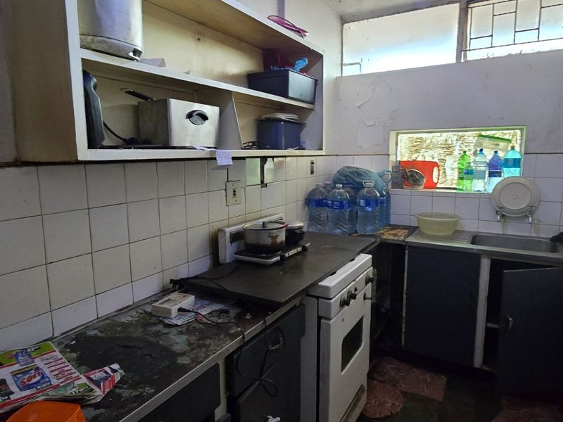 A compact kitchen featuring tiled splashbacks, built-in cabinetry, and a stainless steel sink, currently requiring significant maintenance and cosmetic updates.