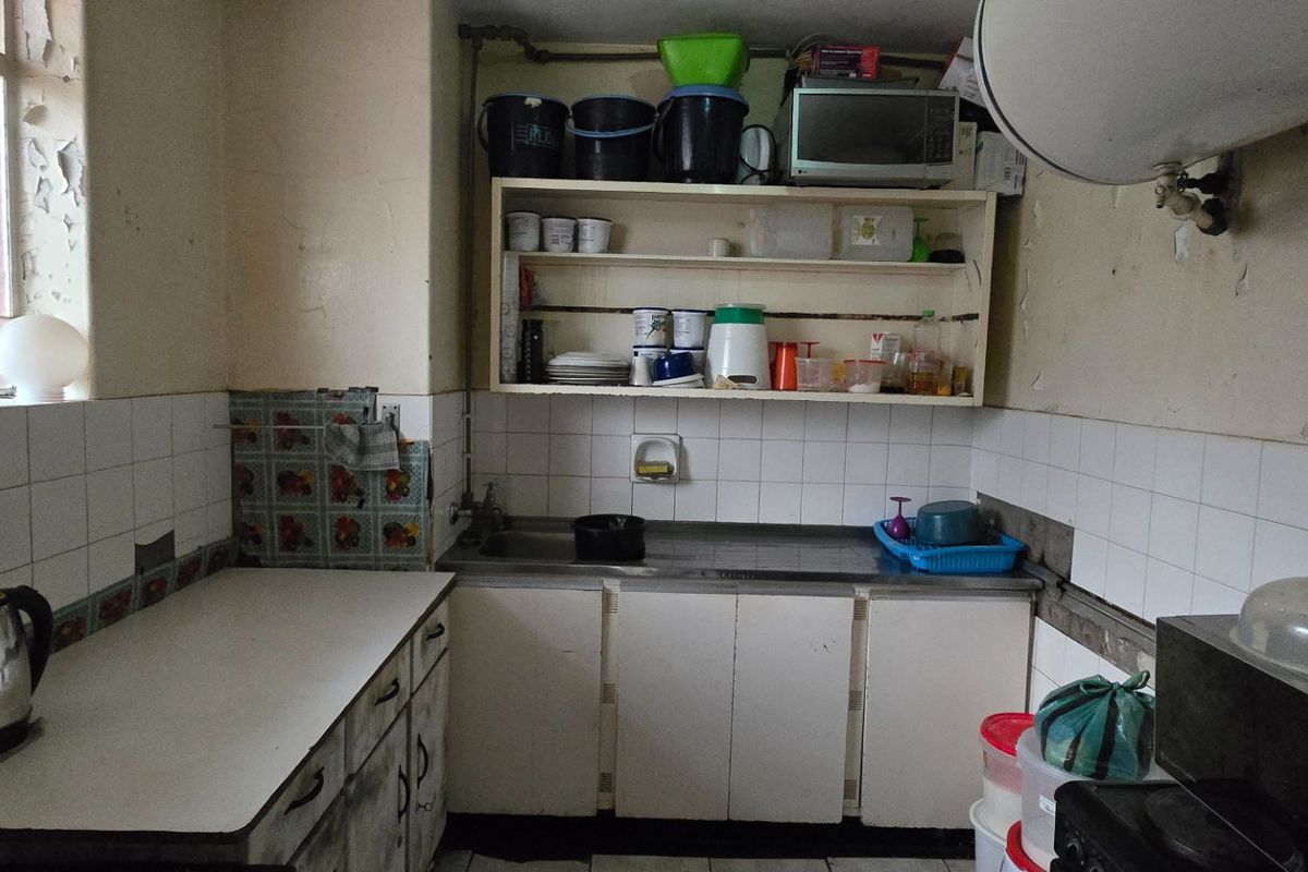 A dated kitchen featuring basic cabinetry, a stainless steel sink, and tiled backsplash, currently showing significant signs of wear and peeling paint.