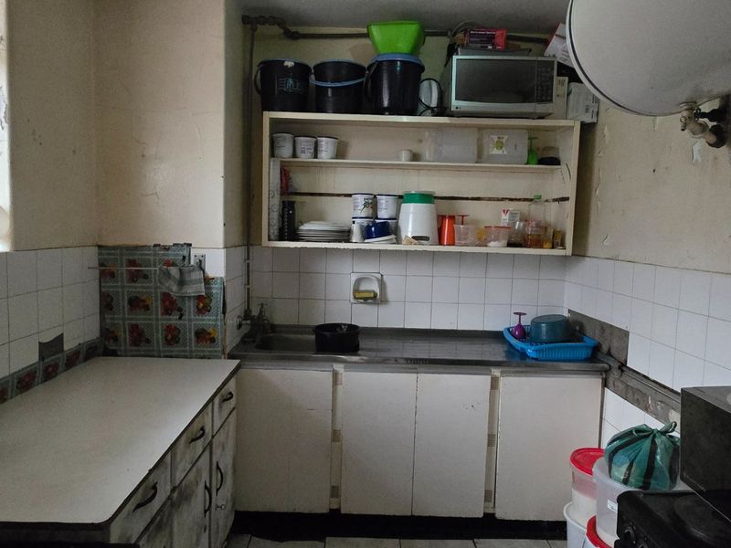 A dated kitchen featuring basic cabinetry, a stainless steel sink, and tiled backsplash, currently showing significant signs of wear and peeling paint.