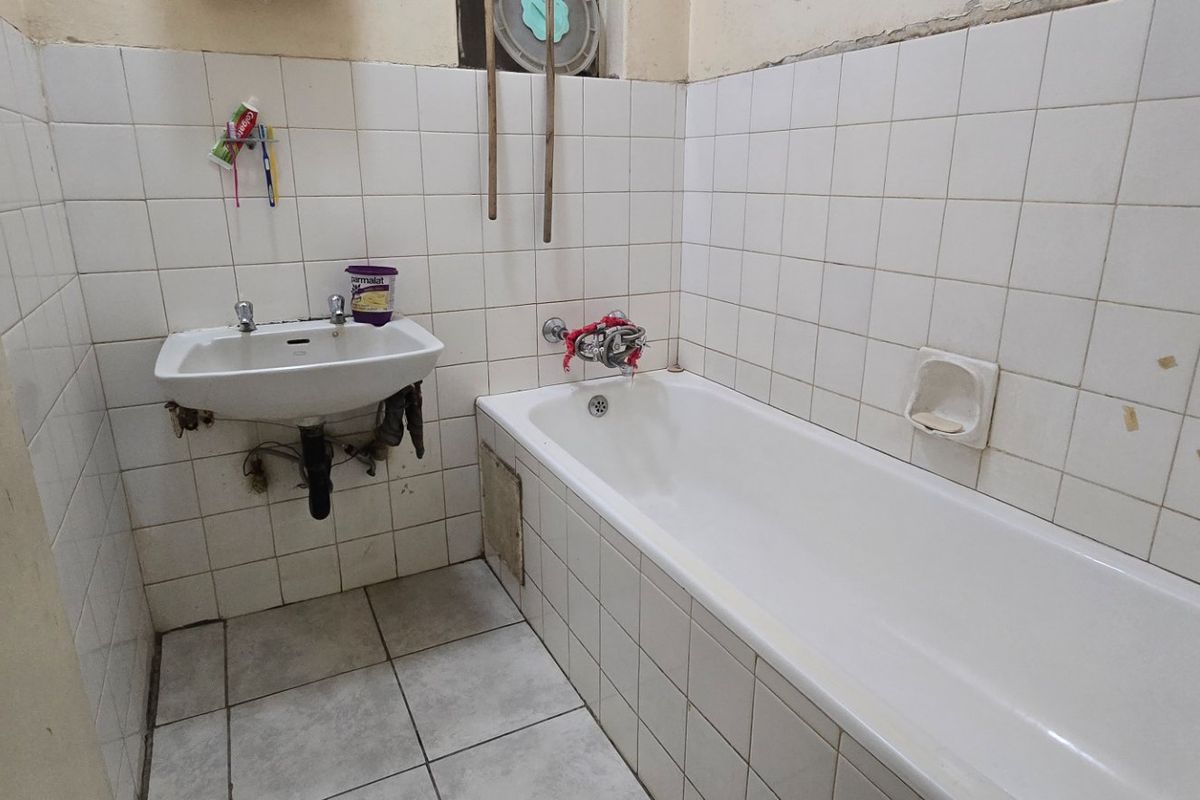 A dated bathroom featuring a wall-mounted basin and a built-in bathtub with white ceramic wall and floor tiling.