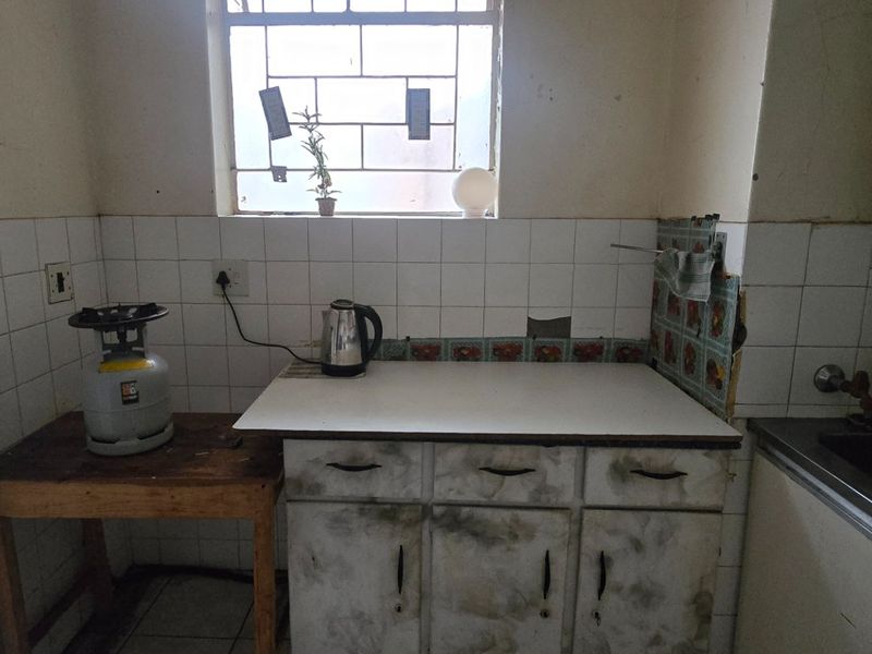A dated kitchen area featuring original cabinetry, tiled splashbacks, and a stainless steel sink, requiring renovation to modernize the space.